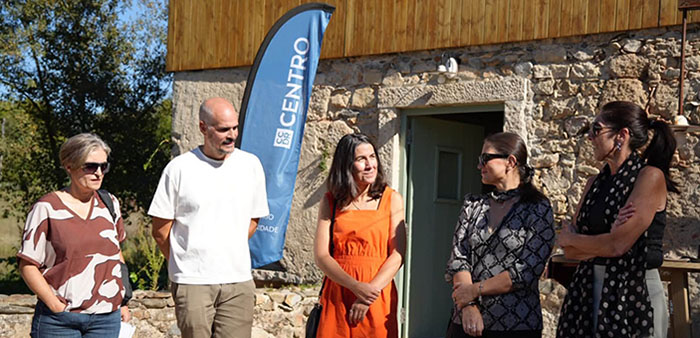 cinco pessoas em conversa, junto a casa de pedra, com bandeira CCDR Centro no fundo